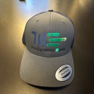 The Moving Edson Baseball Cap is a gray mesh snapback with the MEA logo in blue and green, "moving edson & area" embroidered on the front, and a Yupoong Snapback sticker, displayed on a dark surface.
